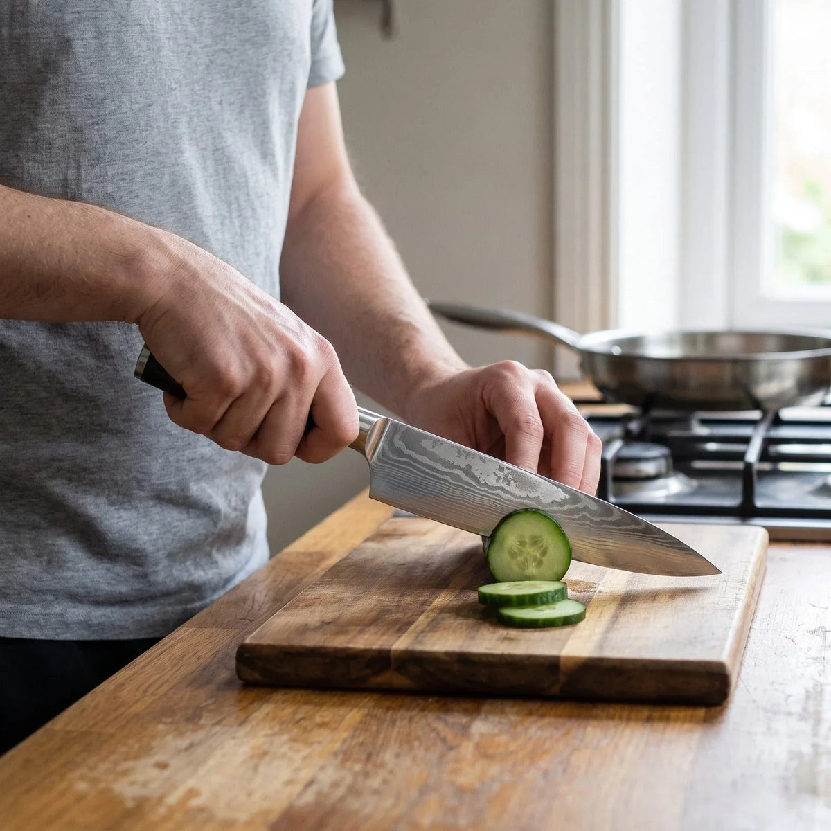 Chef knife in use slicing cucumber on a wooden board